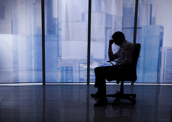 Tensed Businessman Sitting On Chair By Office Window