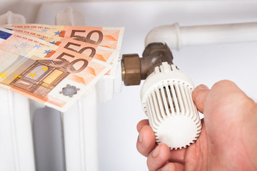 Man Adjusting Thermostat By Euro Notes