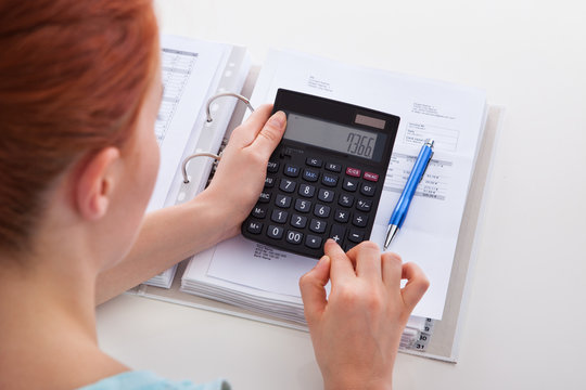 Woman Calculating Invoice At Desk