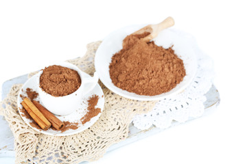 Cocoa powder in cup on napkin on wooden board isolated on white