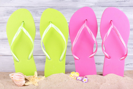 Bright flip-flops on sand, on wooden background