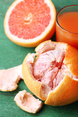 Ripe grapefruits and juice in glass on color wooden background