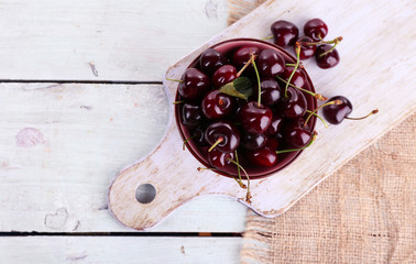 Sweet cherries in color bowl and mug on wooden background