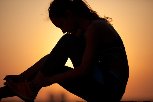woman tying shoelaces against yellow sky at sunset