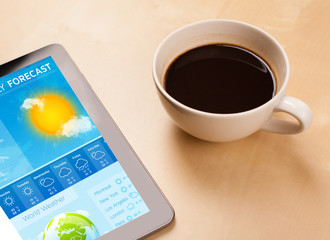 Tablet pc showing weather forecast on screen with a cup of coffe