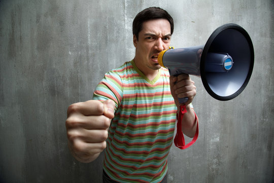man yells into a megaphone and showing fist, against a gray text