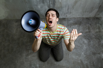 man kneeling and holding a megaphone, begs, against a gray textu