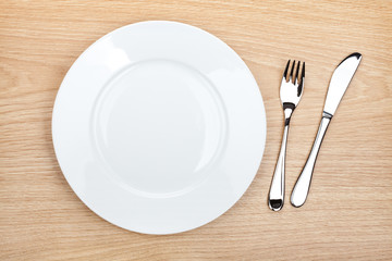 Empty white plate with silverware on wooden table