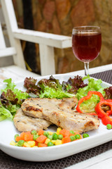 Grilled pork on white plate with glass of wine