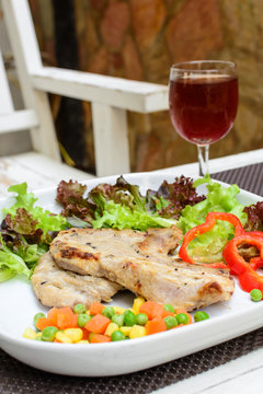 Grilled pork on white plate with glass of wine