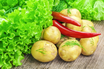 Fresh potatoes with lettuce and peppers on table