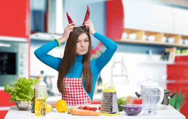 Funny portrait of a young woman with pepper horns in the kitchen