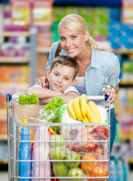Mother and son with cart full of products in market