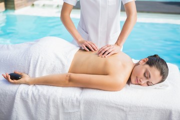 Obraz na płótnie Canvas Happy brunette getting a hot stone massage poolside