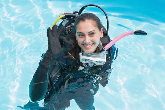 Smiling woman on scuba training in swimming pool making ok sign