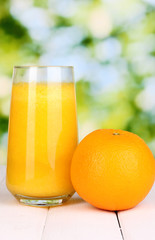 Glass of fresh orange juice on wooden table, on green