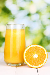 Glass of fresh orange juice on wooden table, on green