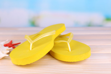 Bright flip-flops on wooden table, on nature background
