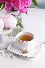 Composition of beautiful peonies in vase, tea in cup and