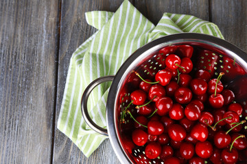Sweet cherries in colander on color wooden background