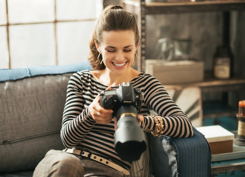 Happy woman sitting on divan and using modern dslr photo camera