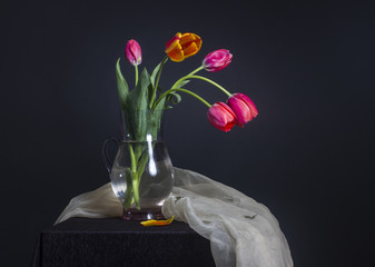 red tulips in a glass jug on black background.