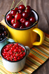 Summer berries in color mugs on color wooden background