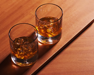 Highball whiskey glass with ice on wooden background.