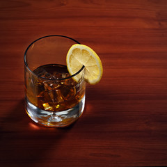 Highball whiskey glass with ice and lemon on wooden background.