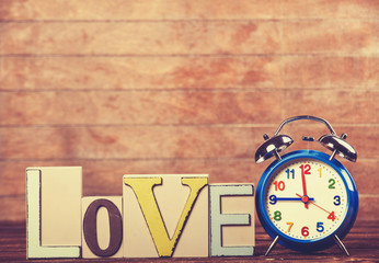 Alarm clock and word Love on wooden table.