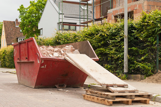 Ein gef&uuml;llter roter Bauschuttcontainer vor einer Hausbaustelle