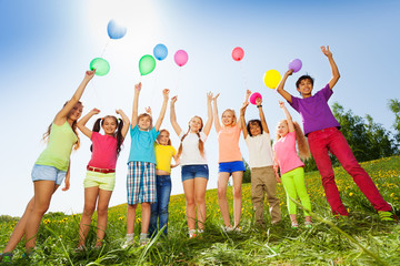 Children standing with arms up to flying balloons