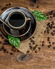 black coffee with beans and green leaves on wooden background