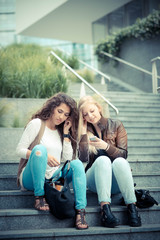 Young women using smartphones and listening to music while sitting on steps