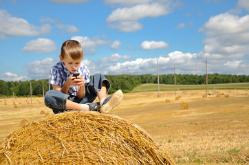 Naklejka na ściany i meble young boy sitting on haystack with phone
