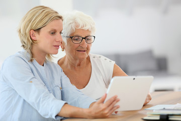 Homehelp with elderly woman using digital tablet - obrazy, fototapety, plakaty