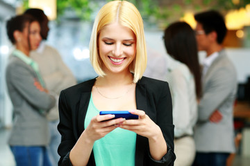 Happy businesswoman using smartphone in front of colleagues