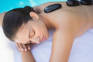 Obraz na płótnie Canvas Relaxed brunette lying poolside having a hot stone massage