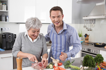 Hotel mama: young man and older woman cooking together pork.