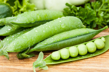 green peas pods lying with greenery
