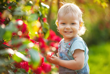 Happy baby boy with flower outdoors in summer garden