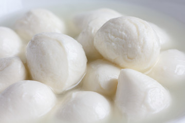 Fototapeta na wymiar Small white mozzarella balls in a white dish with liquid.