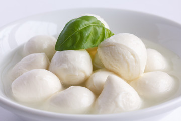Small white mozzarella balls in a white dish with liquid.