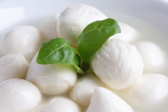 Small white mozzarella balls in a white dish with liquid.
