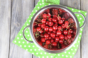 Sweet cherries in colander on color wooden background