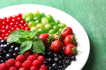 Forest berries on plate, on color wooden background