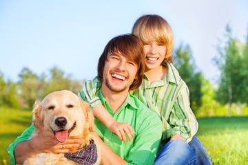 Smiling boy, father and dog sit in park on grass