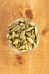 green cardamom in glass bowl on wooden background close-up