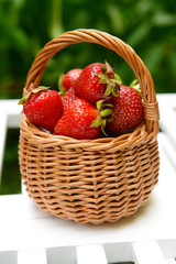 Ripe sweet strawberries in wicker basket on table in garden