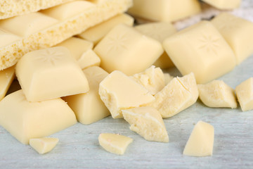 Broken white chocolate bar on color wooden background